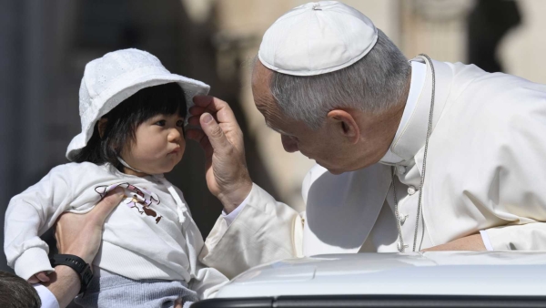 Pope Leo XIV blesses a baby as he rides in the popemobile 